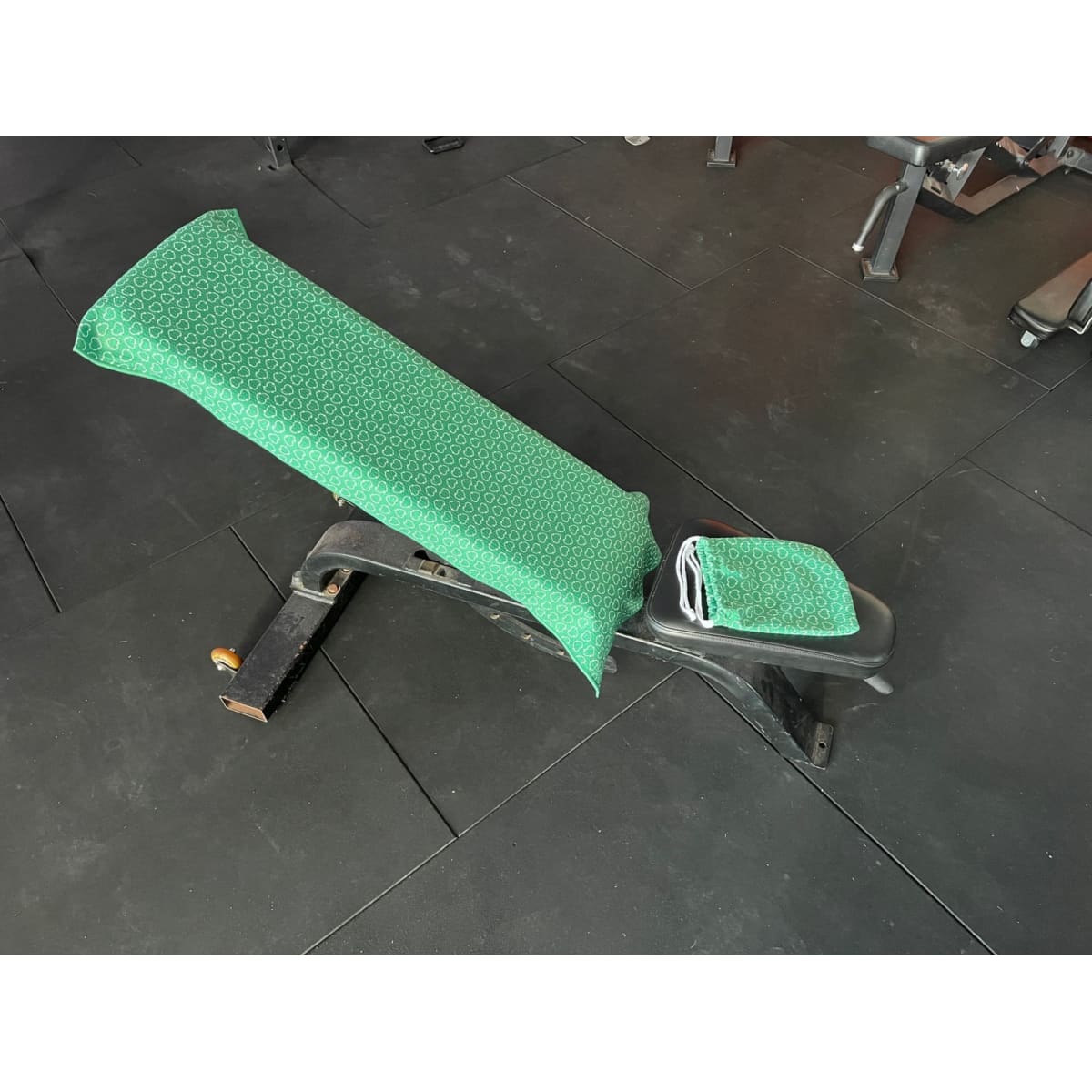 A gym bench covered with a green patterned towel. The towel drapes over the backrest and seat area.