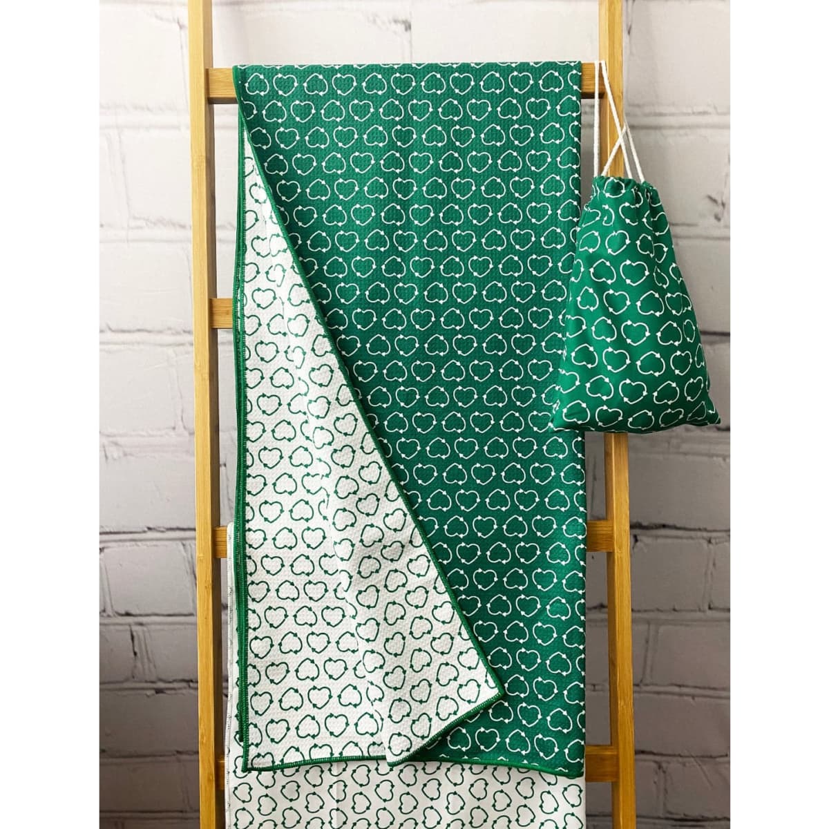 A green beach towel with a cloud pattern, displayed on a wooden rack alongside a matching carry pouch.