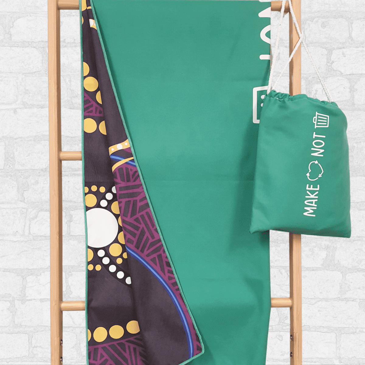 A lightweight green suede towel hangs on a wooden rack, showing a patterned underside and a matching carry bag.