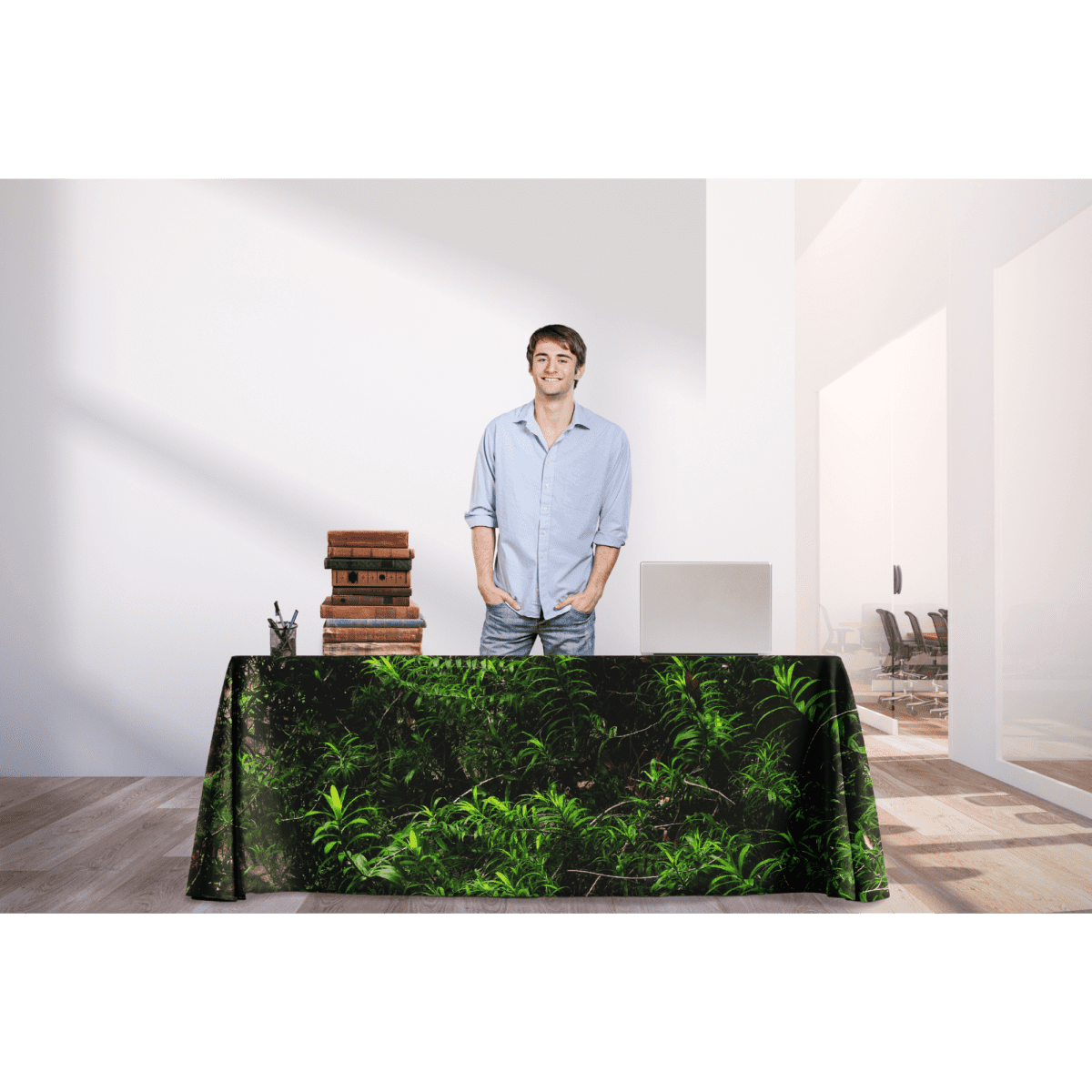 A man stands behind an 8ft table covered with a green rPET throw featuring a botanical design, in a modern indoor space.