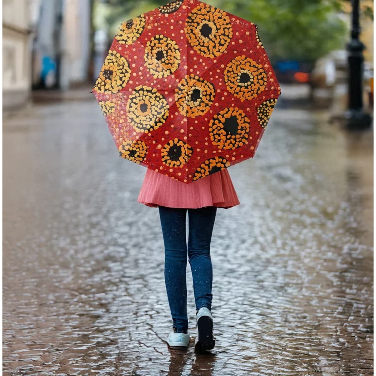 A red umbrella with a floral pattern, held by a person walking on a wet cobblestone street.