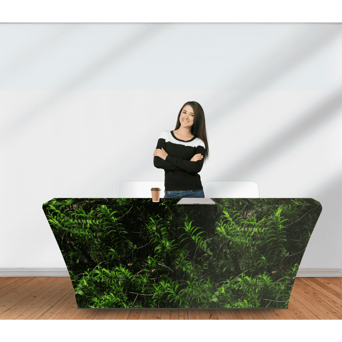 A table cover with a vibrant green fern design, draped over a modern, angular table. A woman stands casually beside it.