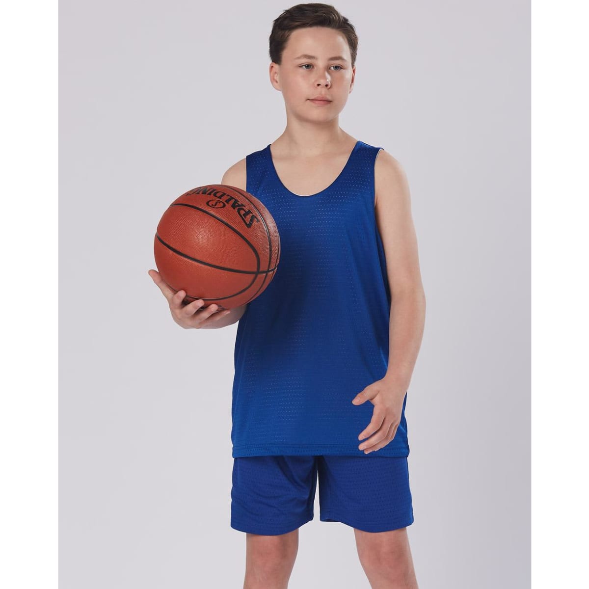 A boy wearing blue basketball shorts and a matching sleeveless top, holding a basketball. The outfit features a logo.
