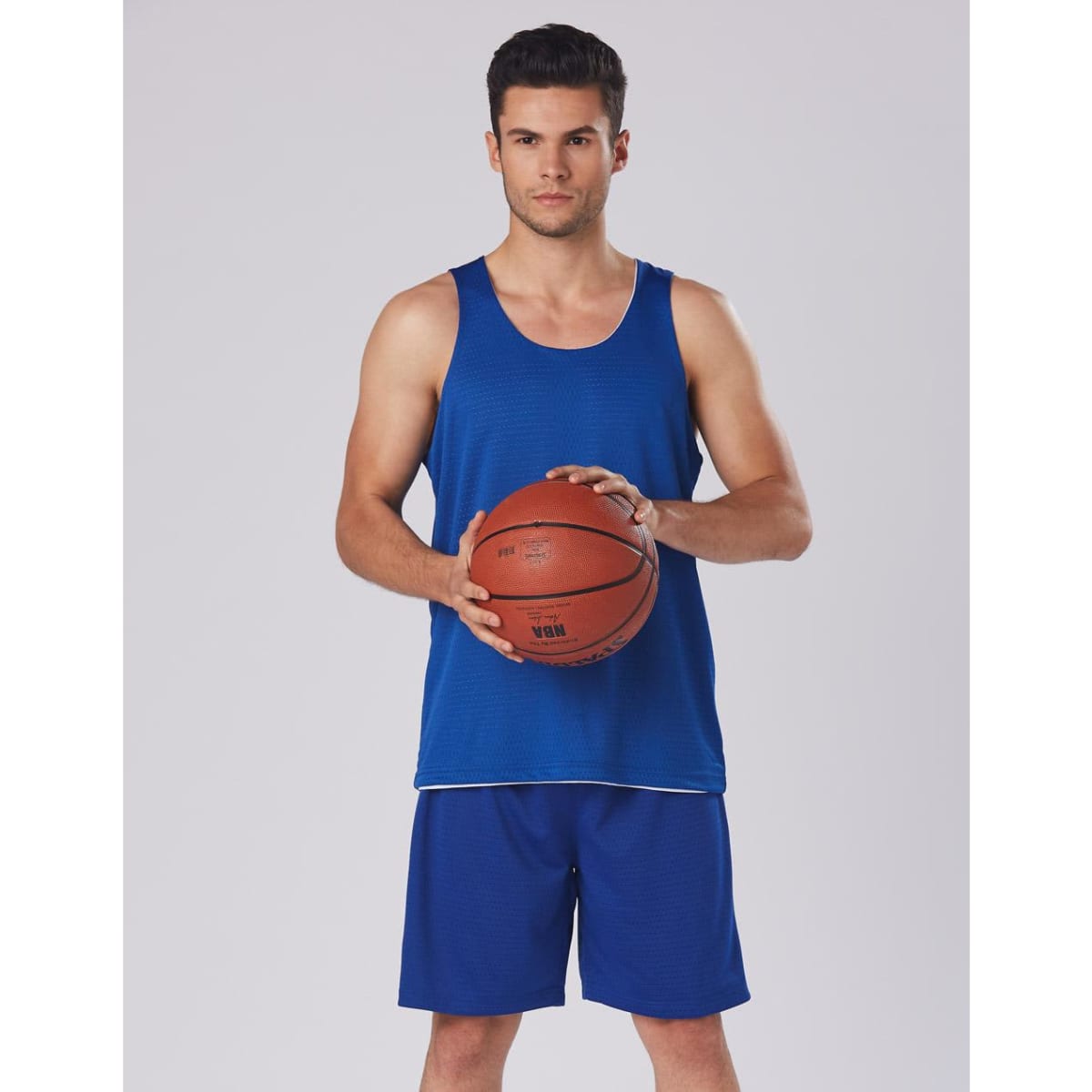 A person holding a basketball, wearing blue basketball shorts and a blue tank top. The shorts feature a logo.