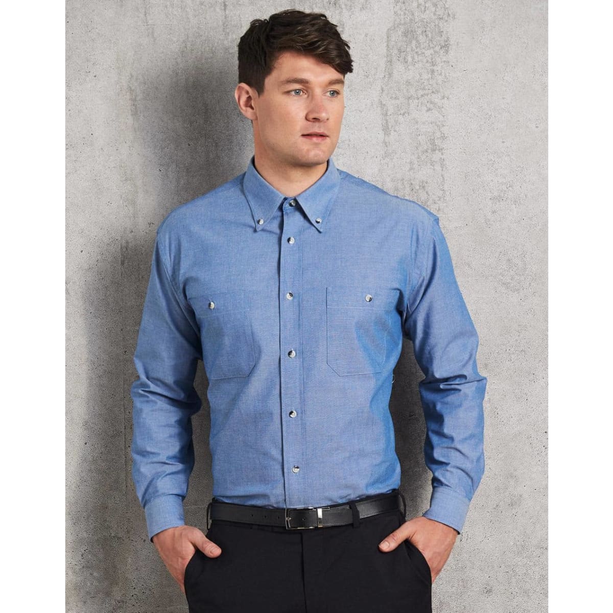 A blue chambray long sleeve shirt with two chest pockets and a button-up front, featuring a subtle brand logo.