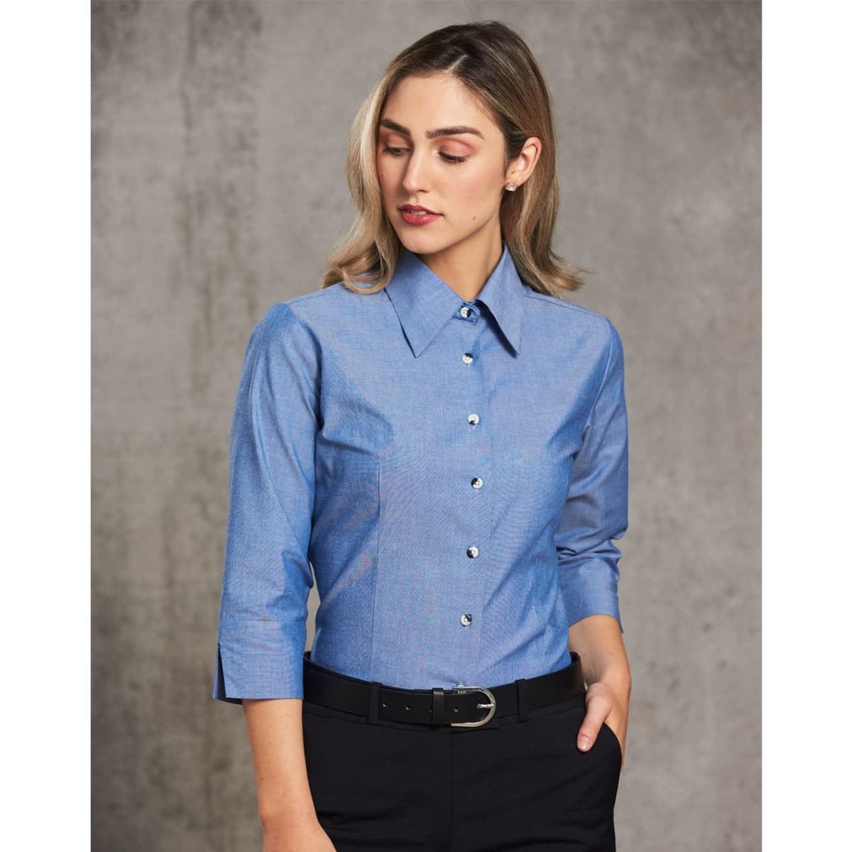 A fitted ladies' chambray shirt in blue with a button-up front and 3/4 sleeves, featuring a simple collar and branding.