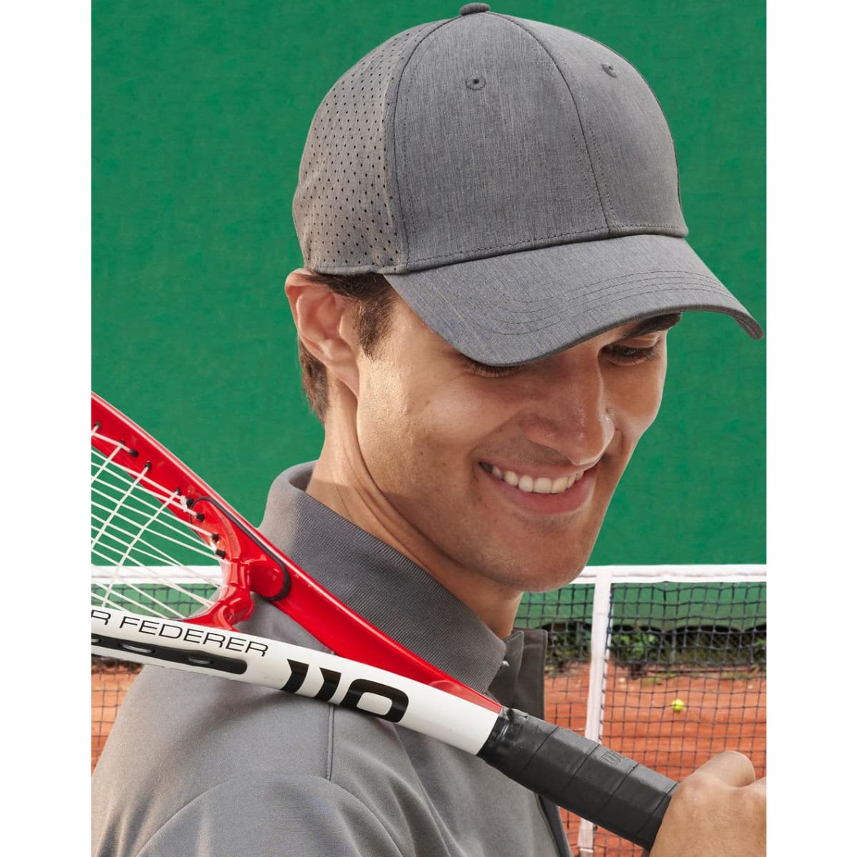 A grey 4-way stretch cap with a perforated design worn by a smiling man holding a tennis racquet.