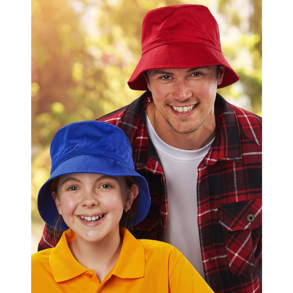 A red bucket hat and a blue bucket hat are worn by a smiling man and girl outdoors. Both hats feature a toggle.