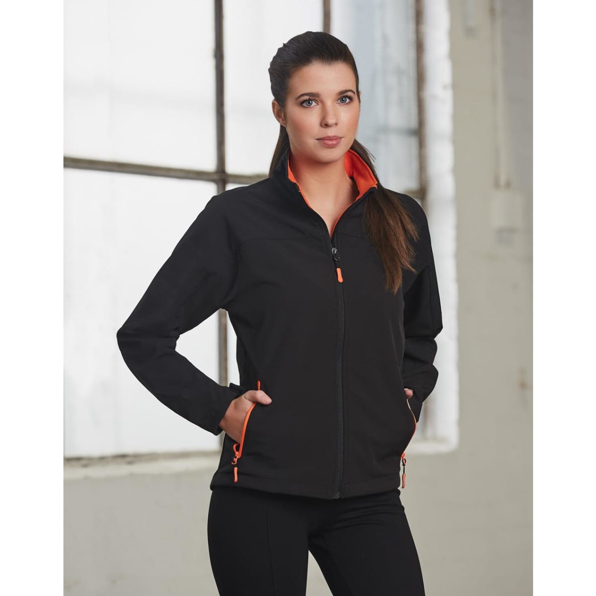 A black softshell jacket with orange contrast detailing, featuring a zippered front and pockets.