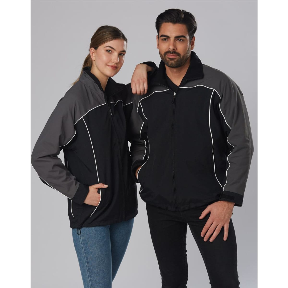 A black and grey reversible jacket featuring a logo, modelled by a man and a woman.
