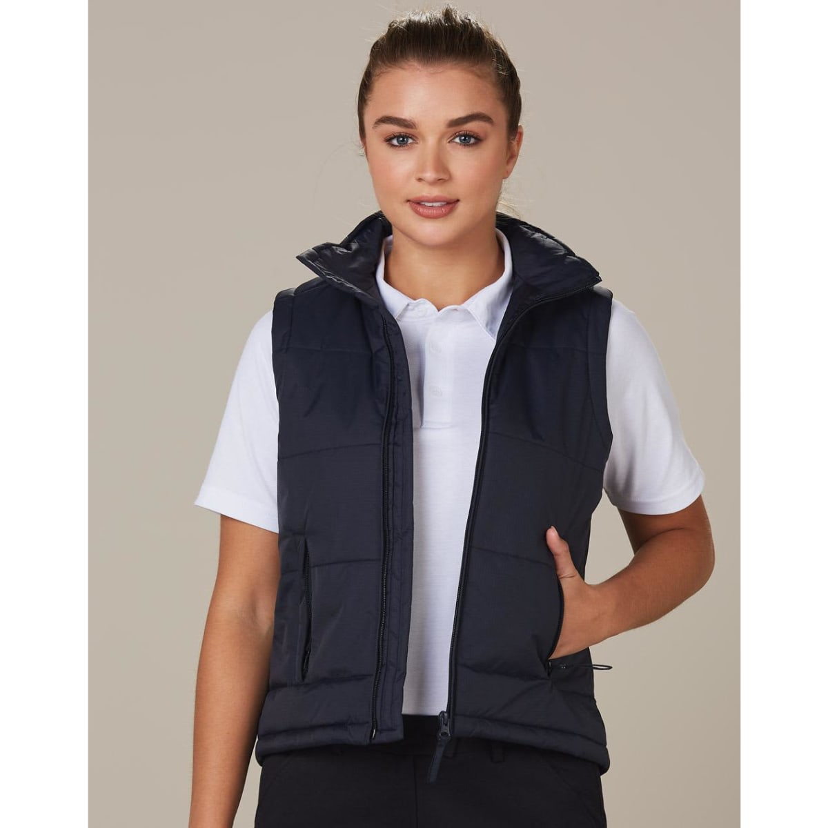 A padded vest in navy blue, featuring a high collar and pockets, worn over a white polo shirt.