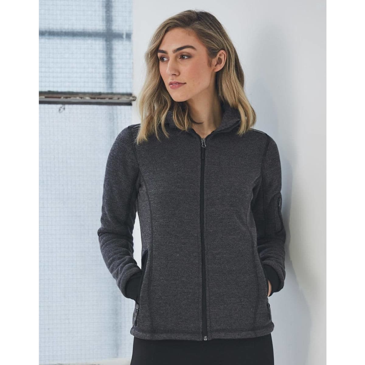 A ladies' heather bonded fleece jacket in dark grey with a zip closure and pockets. The model has a neutral expression.