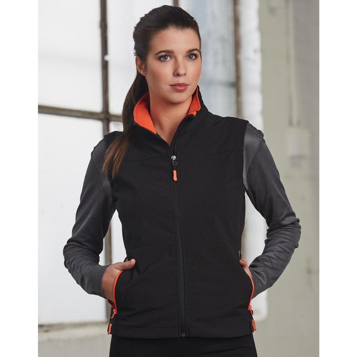 A softshell vest in black and grey with an orange lining and zipper, featuring a logo and pockets.