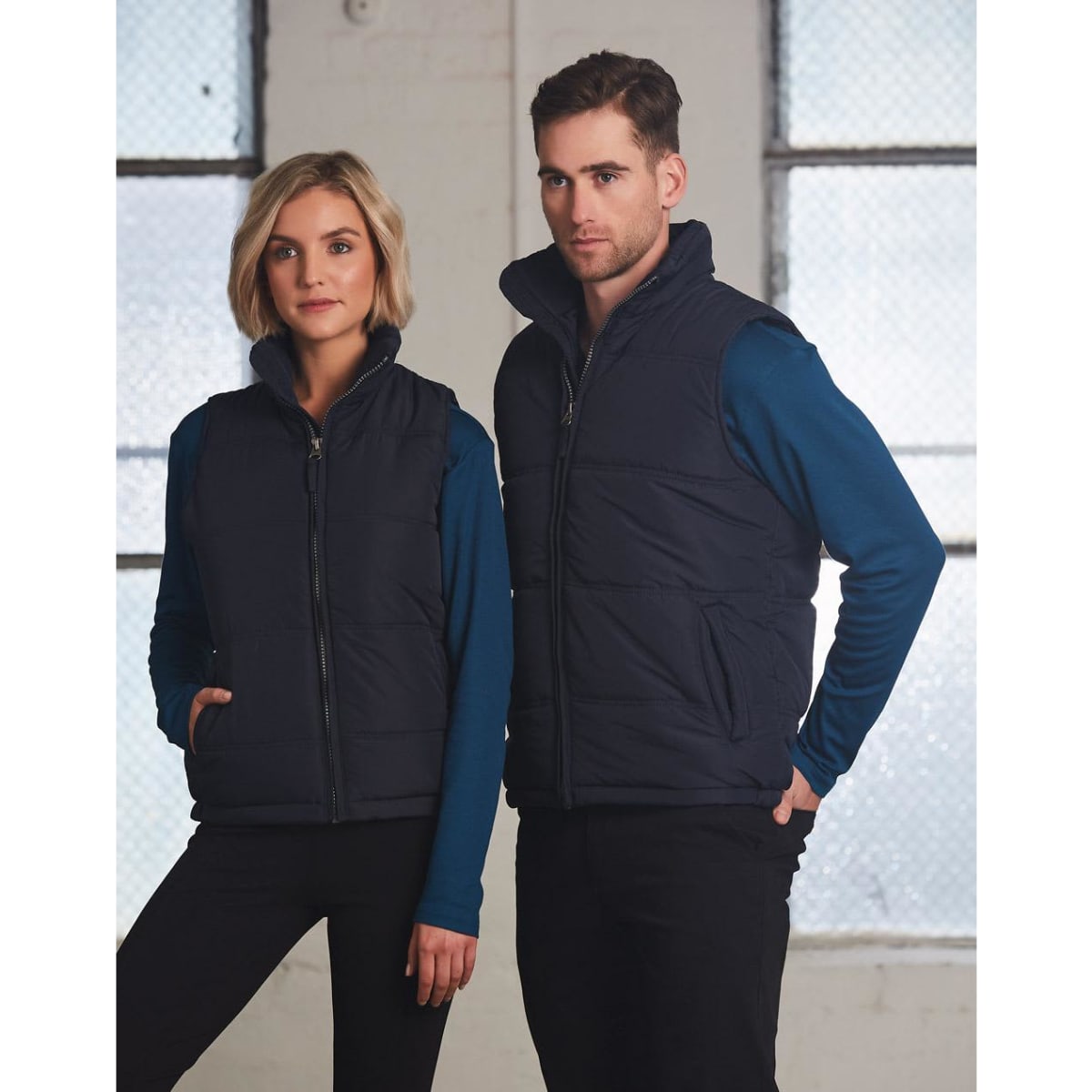 A navy blue heavy quilted vest is worn by a male and female model against a light backdrop, featuring a logo.
