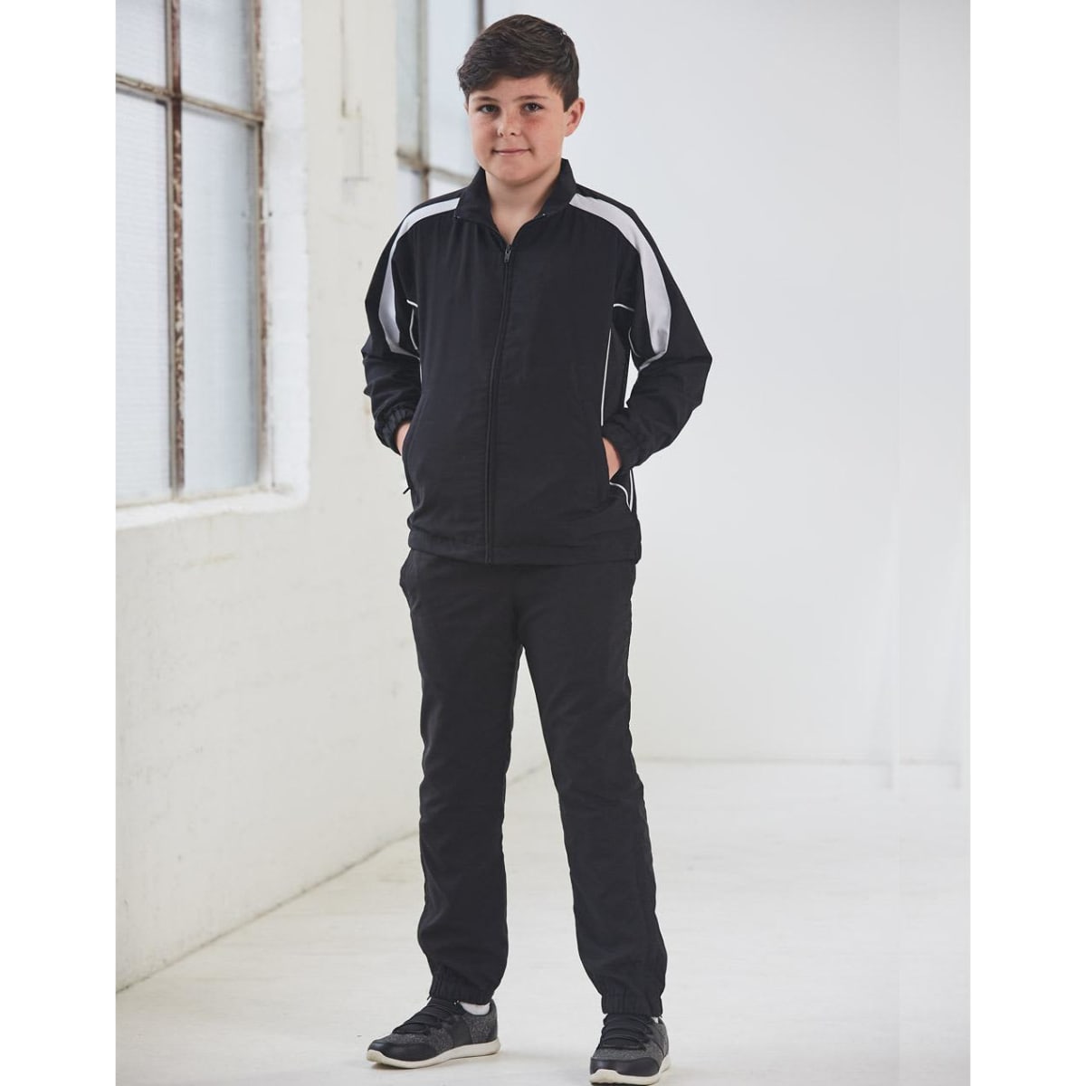 A black track jacket with white accents, featuring a zip front and side pockets, modelled by a young boy.
