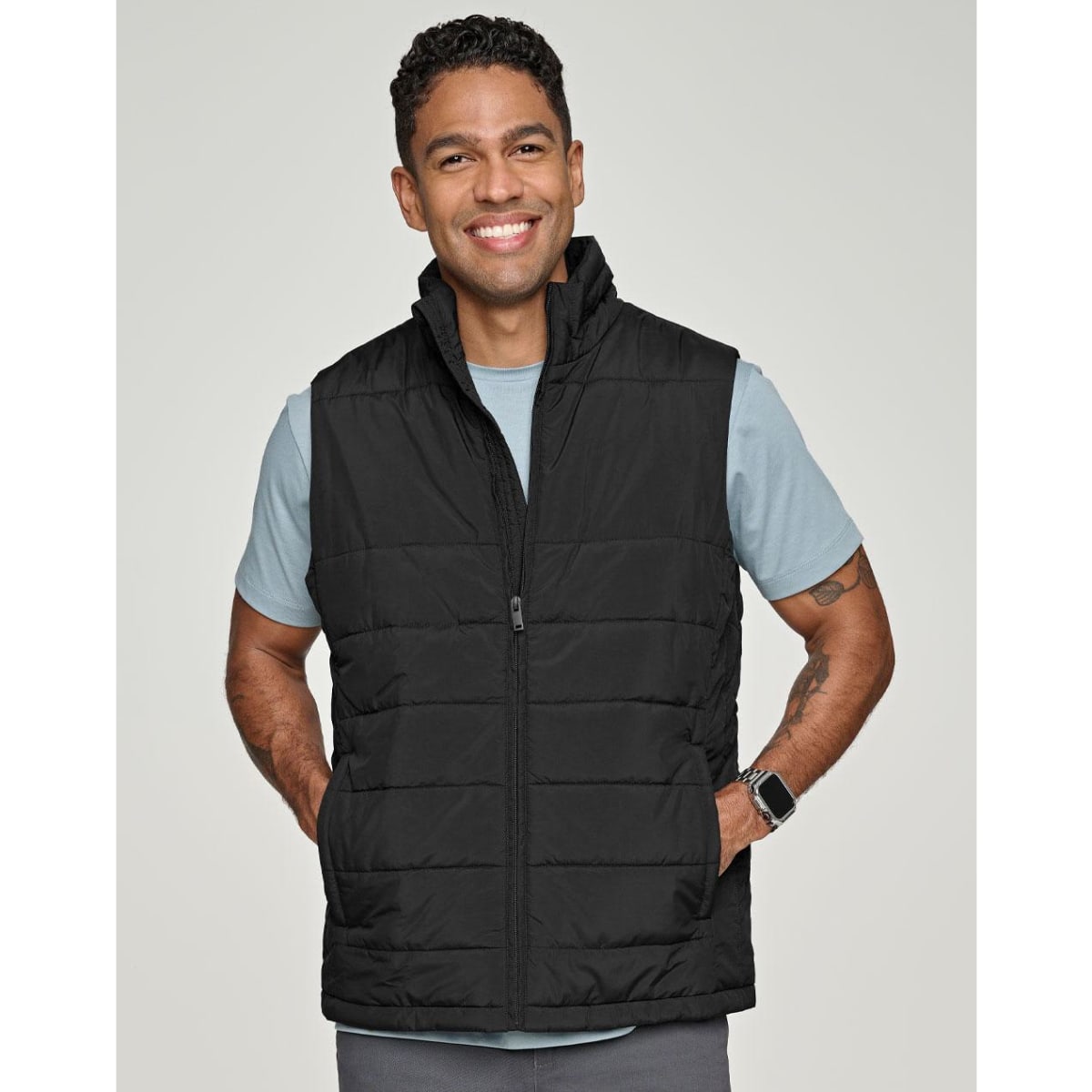 A man wearing a black insulated puffer vest with a 3D cut over a grey shirt, smiling. The vest has a logo.