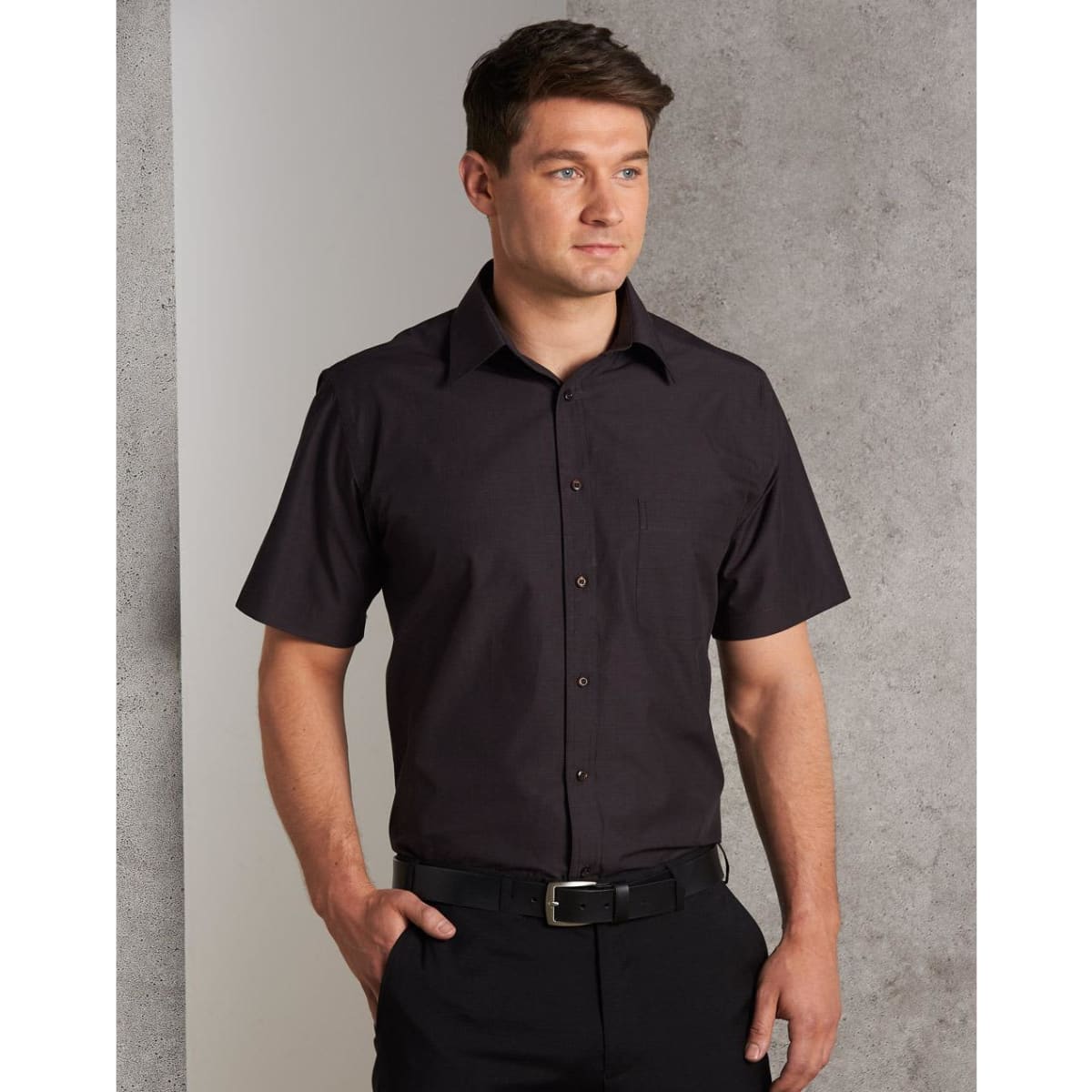 A short sleeve button-up shirt in dark brown, featuring a chest pocket and a collar, worn by a model.
