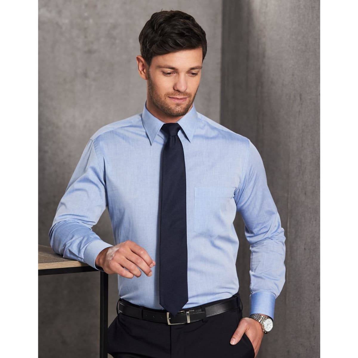 A men's fine chambray long sleeve shirt in light blue, paired with a tie, featuring a chest pocket and a logo.