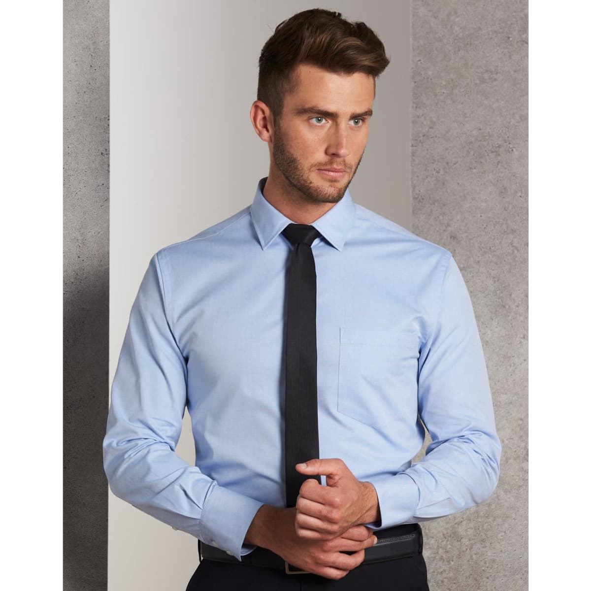 A light blue men's long-sleeve button-up shirt with a chest pocket, styled with a black tie.