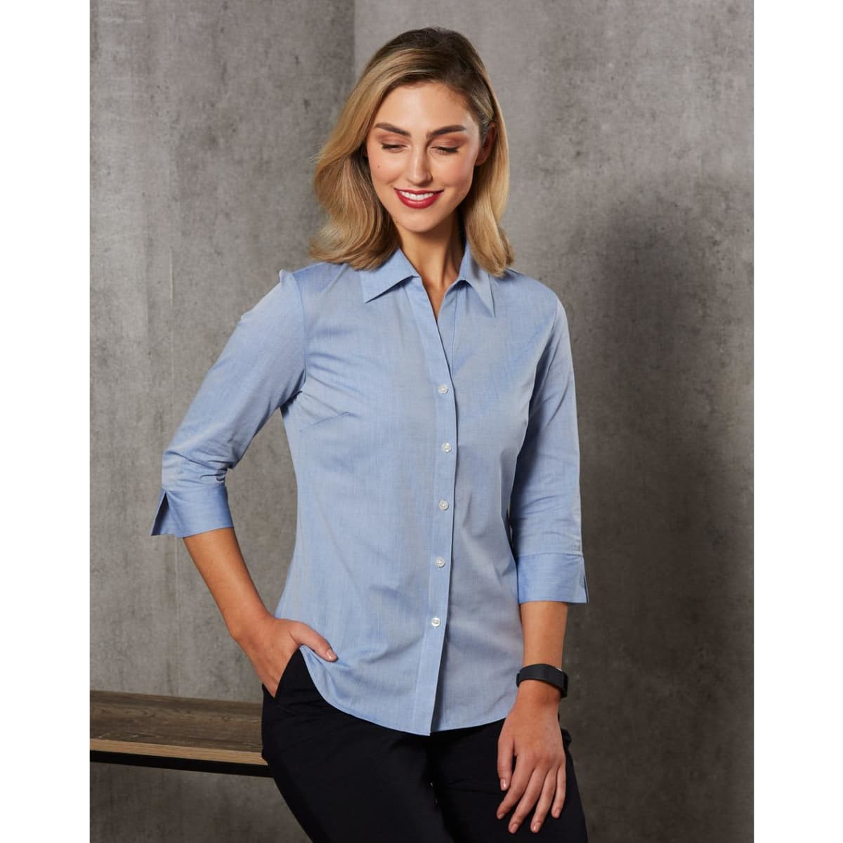 A women's fine chambray shirt in light blue with 3/4 sleeves and a button-up design, featuring a logo.