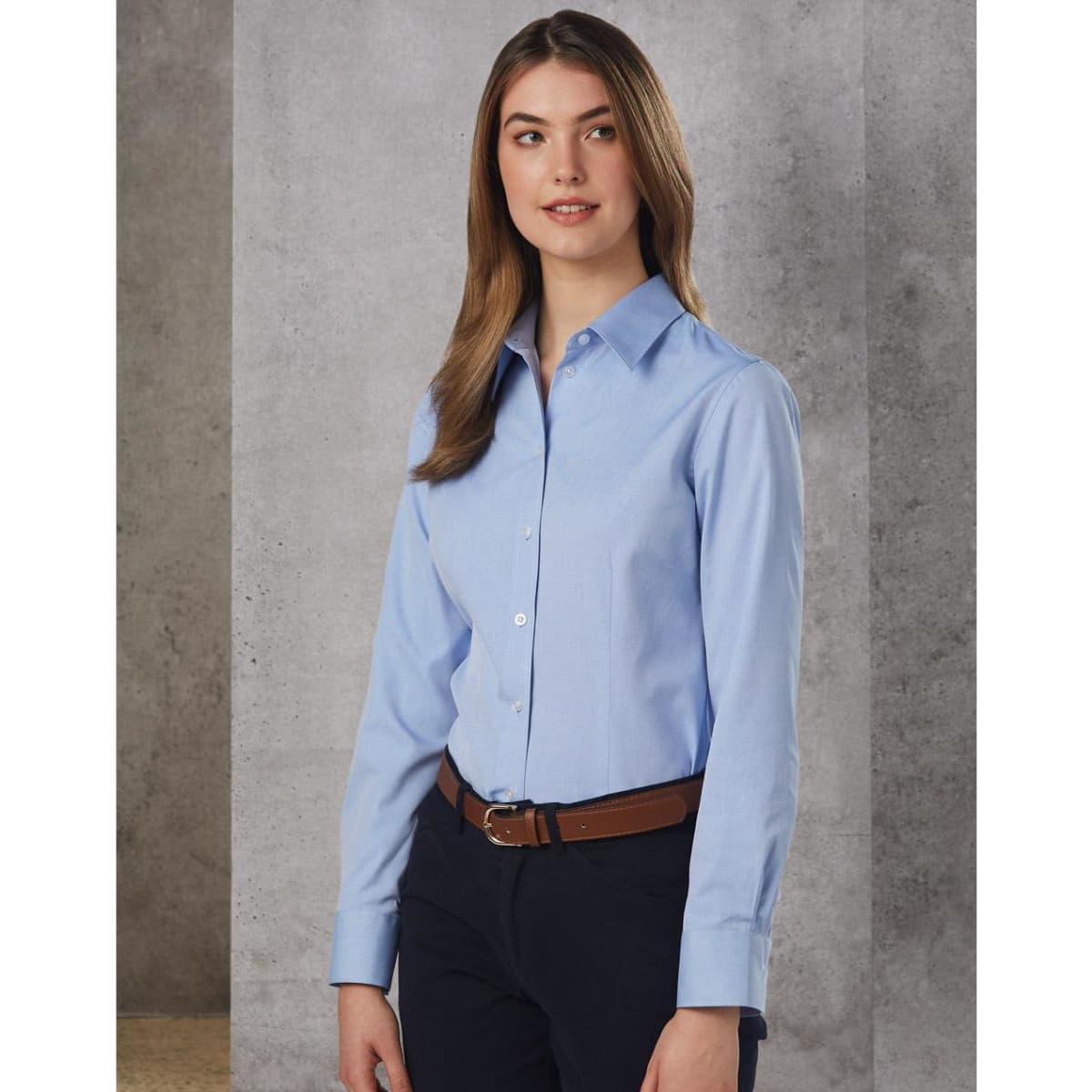 A light blue women's button-up shirt with long sleeves, featuring a collar and a logo, paired with dark trousers.