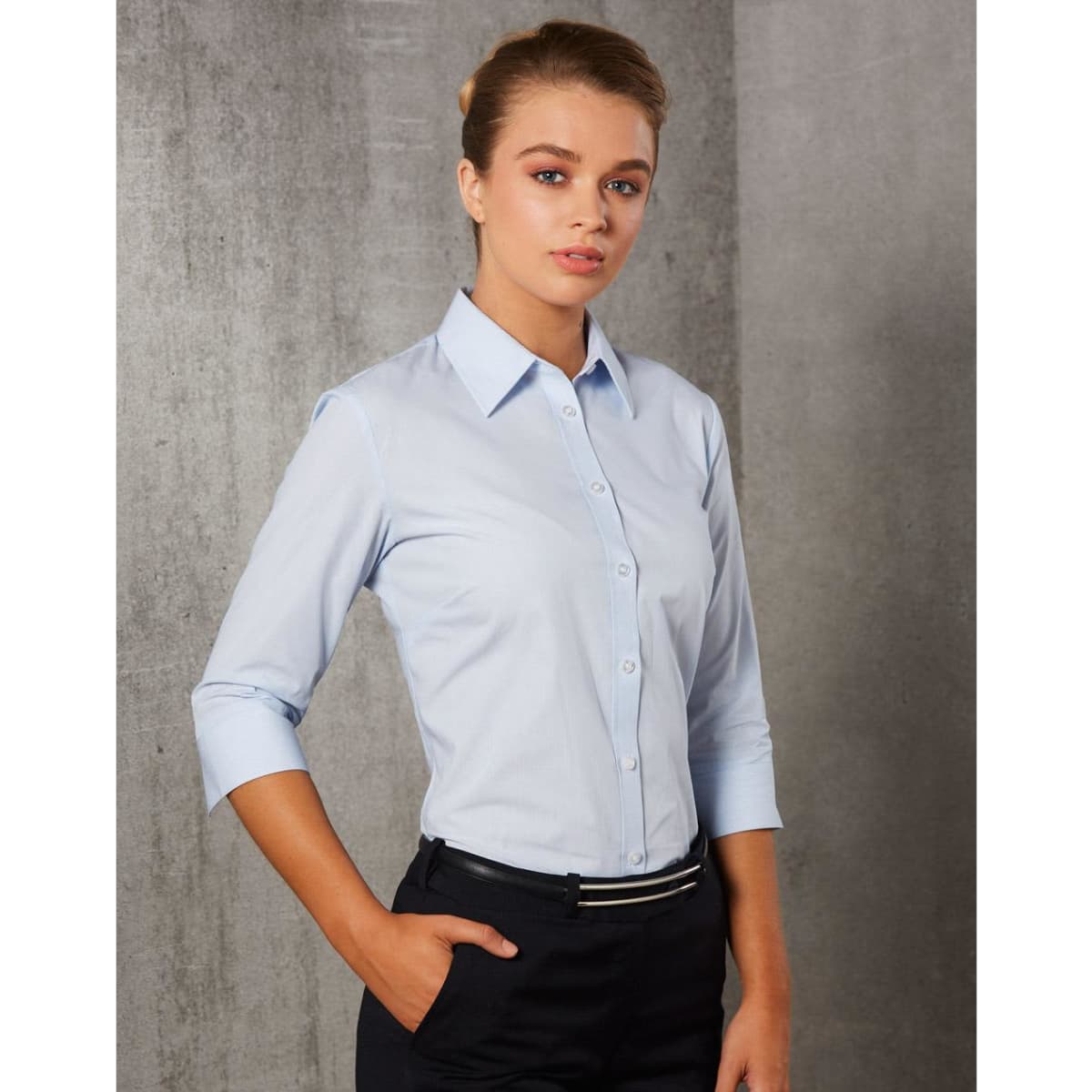 A light blue women's button-up shirt with 3/4 sleeves and a fitted design, featuring a logo on the chest.