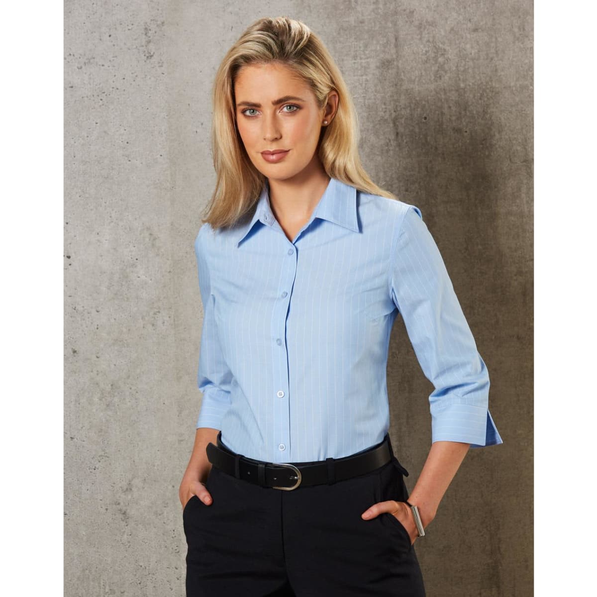 A button-up women's shirt in light blue with pinstripes and 3/4 sleeves, featuring a collar and a fitted design.