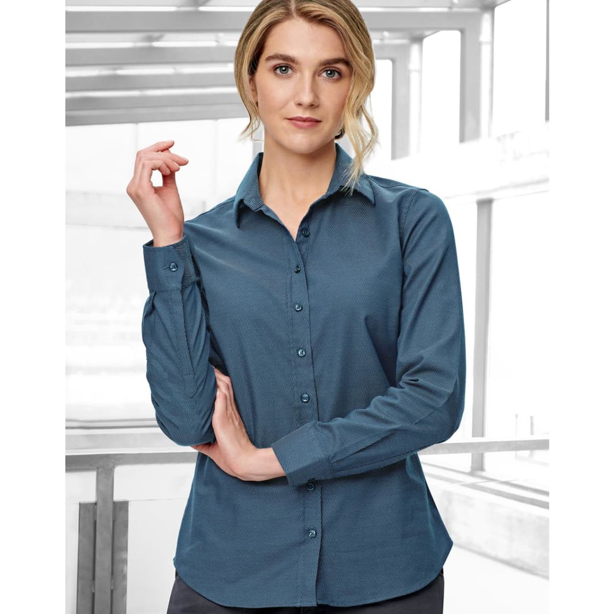 A teal button-up shirt for women with a pin dot pattern and long sleeves, featuring a logo on the chest.