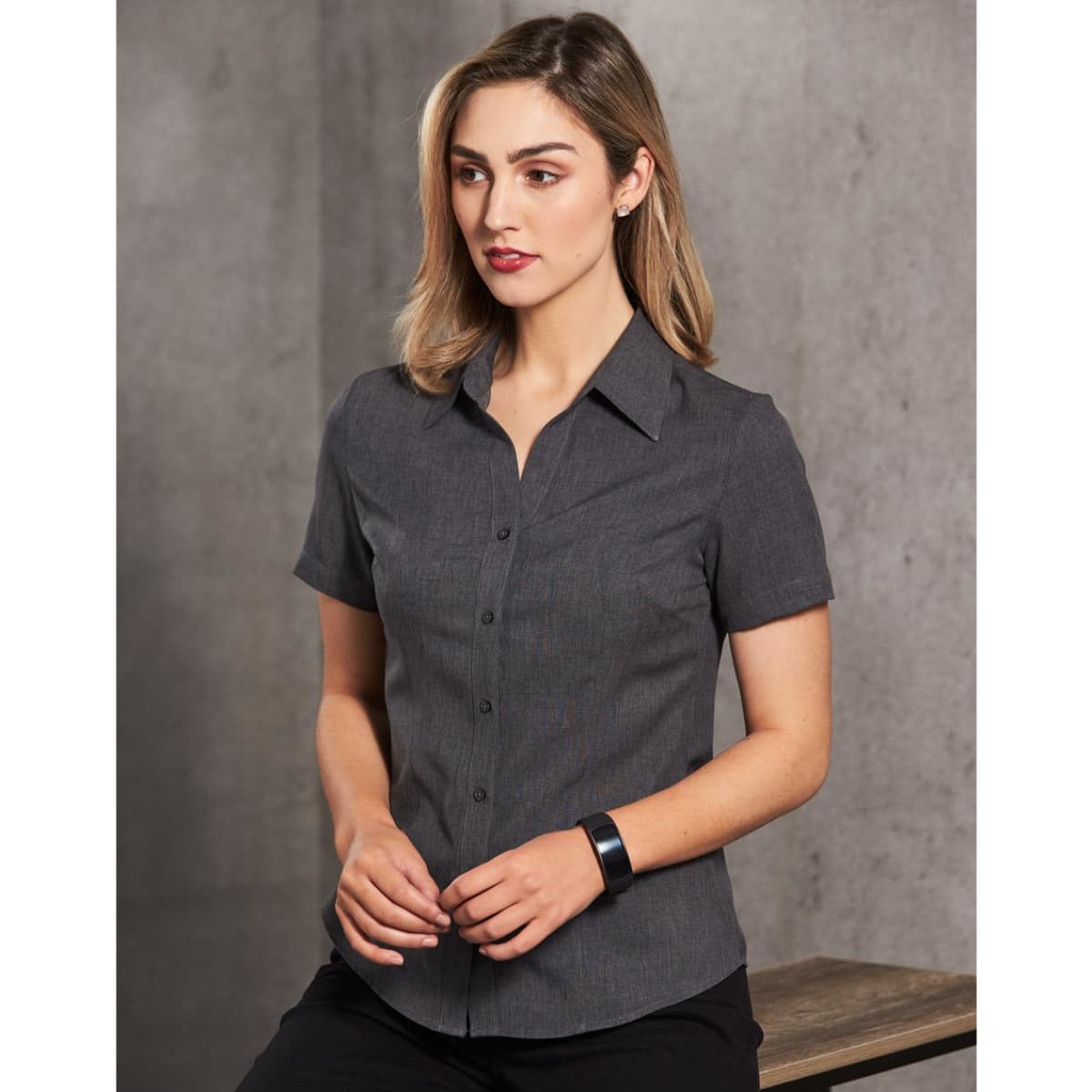 A women's short sleeve shirt in dark grey with a button-up front and collar, featuring a logo.