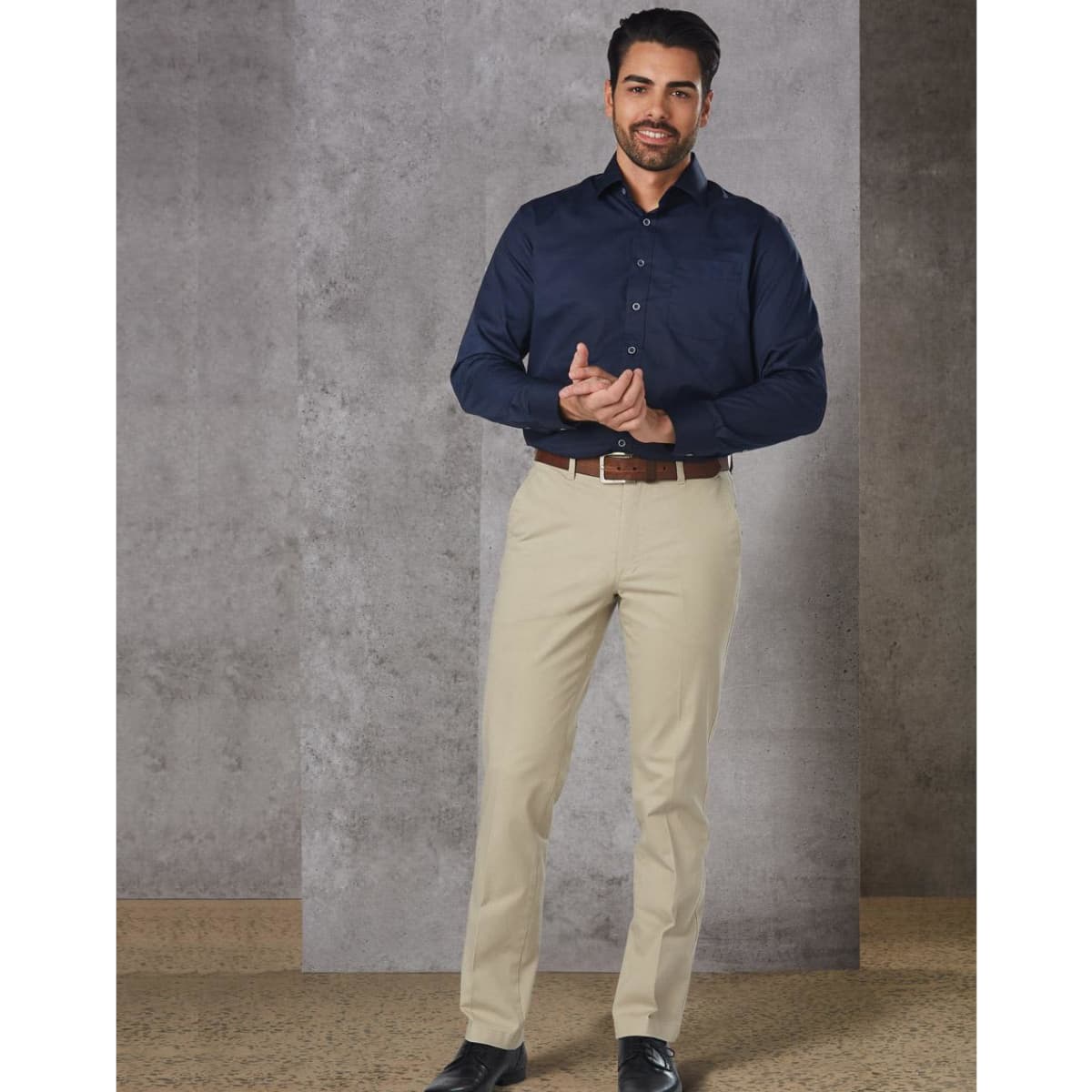 Men's chino pants in a light beige colour, displayed with a navy button-up shirt and brown belt. Features branding on the waistband.