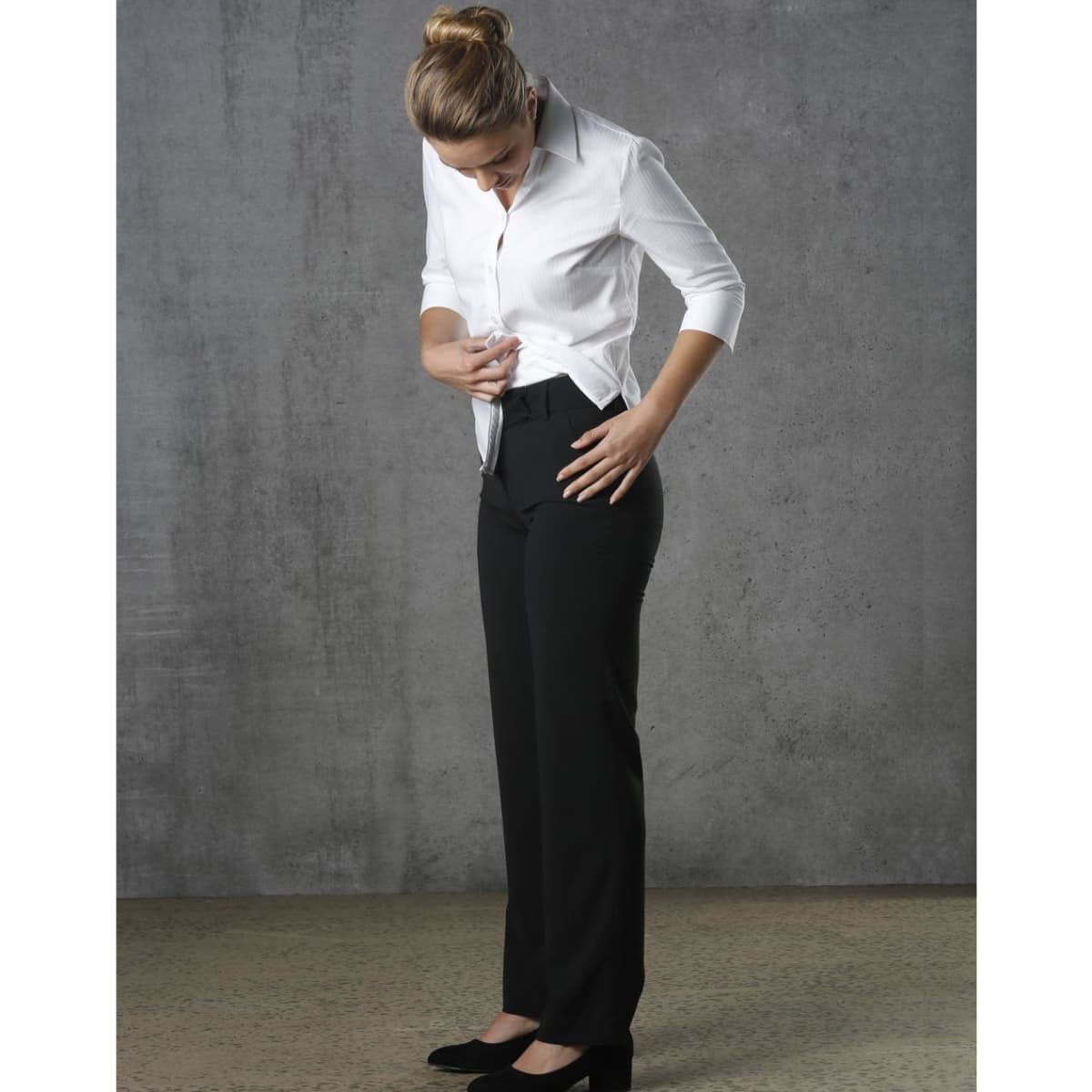 Black low rise pants made from poly/viscose stretch material, paired with a white shirt. The model is adjusting the pants.
