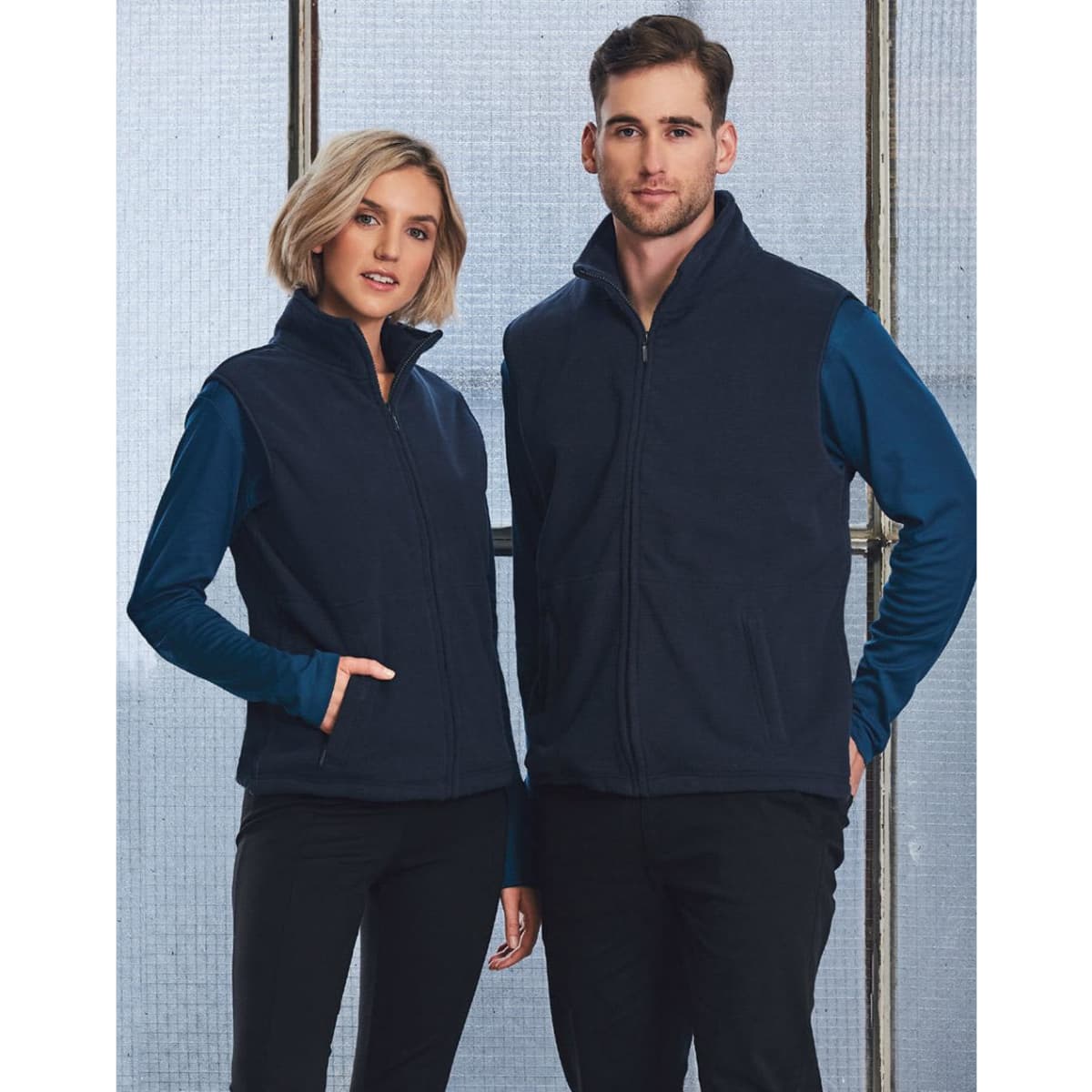 A unisex polar fleece vest in navy blue, worn by a male and female model, features a front zip and pockets.