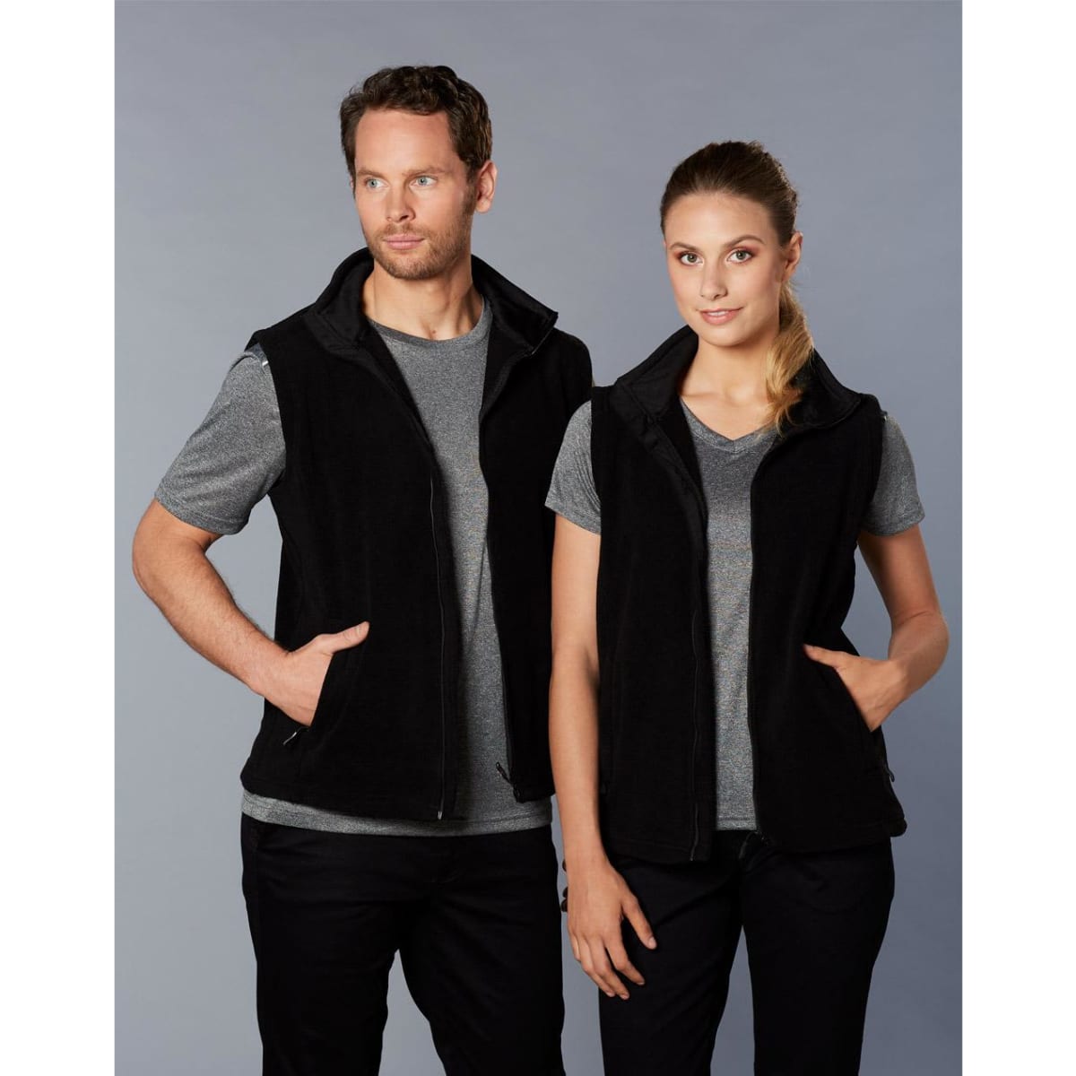 A black polar fleece vest for adults, featuring a zip-up front and side pockets, shown on a man and a woman.