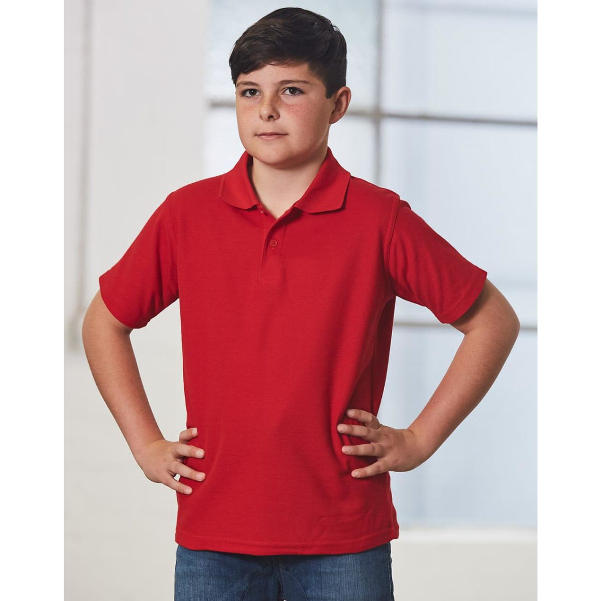A red children's traditional polo shirt displayed on a model, featuring a classic collar and short sleeves.