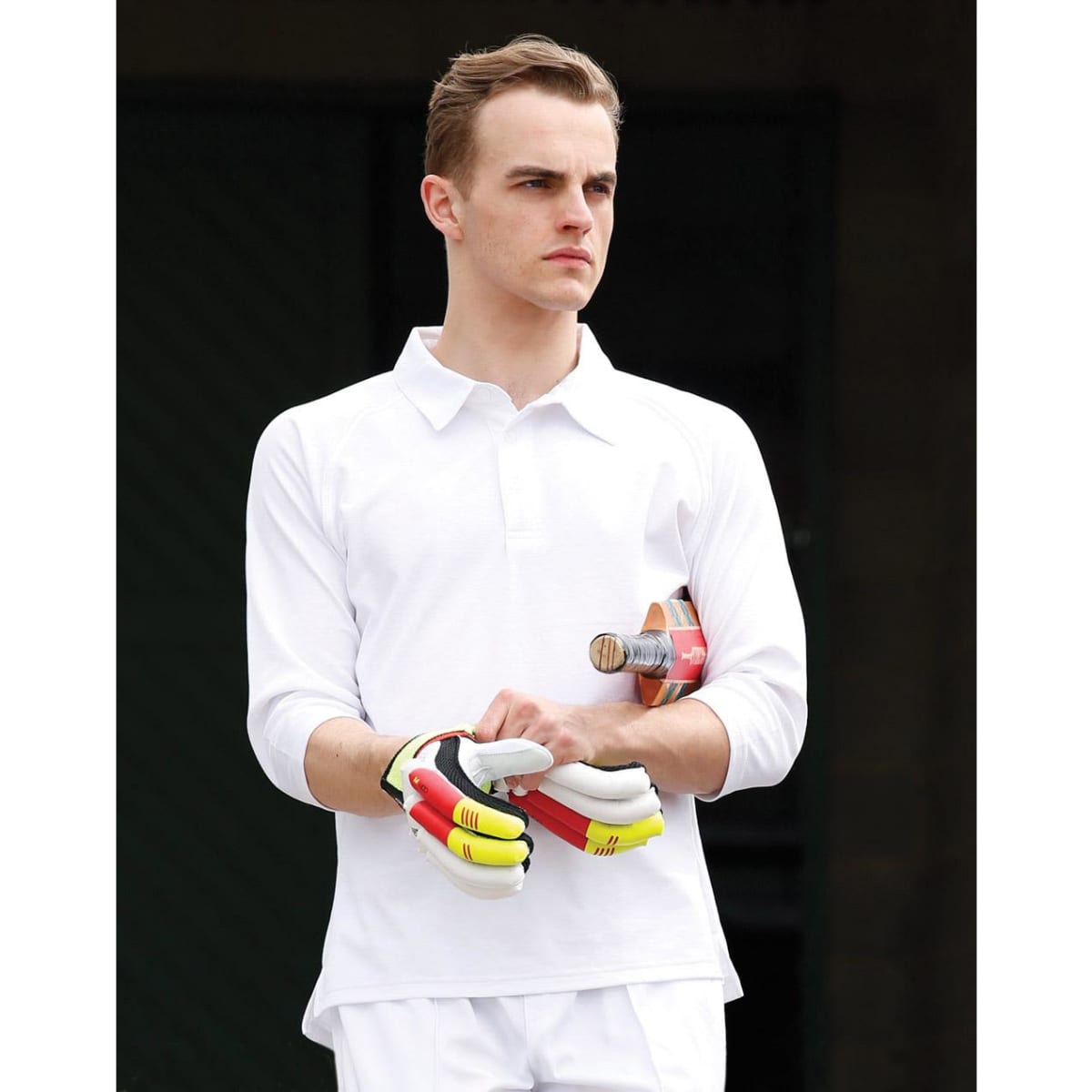 A white men's 3/4 sleeve cricket polo with a logo, worn by a model holding a cricket bat and gloves.