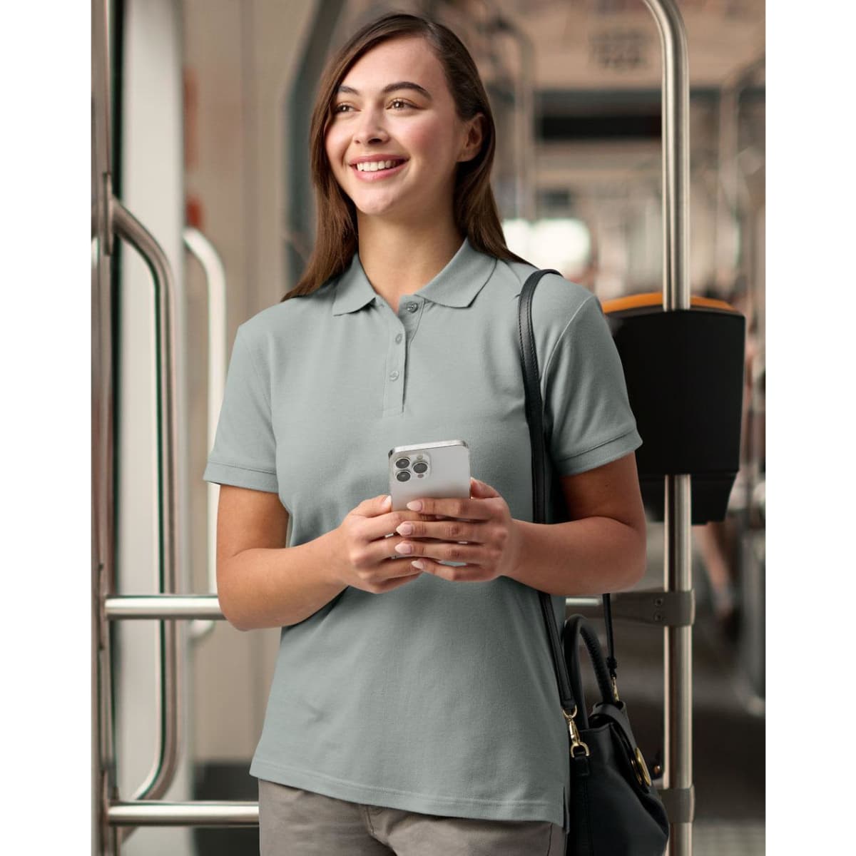 A green women's polo shirt with a fitted design, featuring a collar and buttons, displayed by a model in an industrial setting.