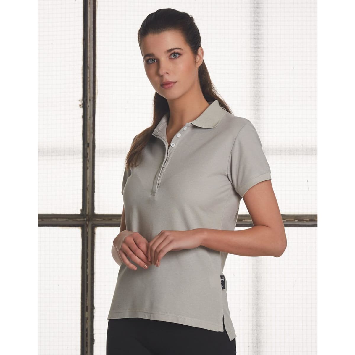 A light grey ladies' polo shirt with a collar and a button placket, featuring a logo on the side.