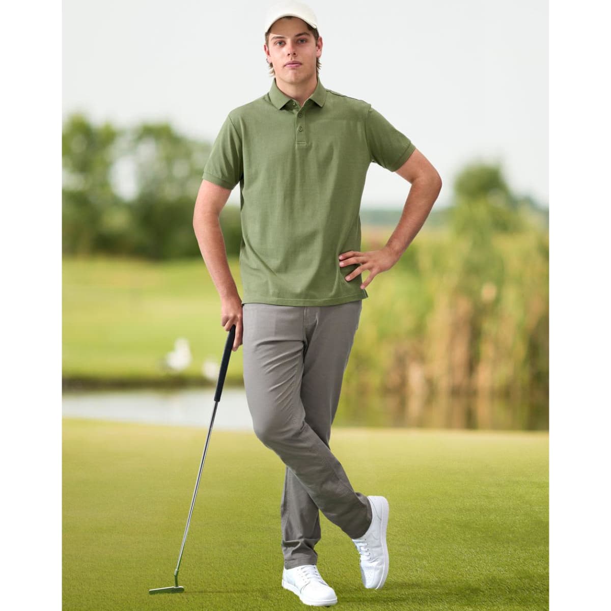A man wears a green ultrafine cotton pique polo with grey pants and white shoes, standing on a golf course.