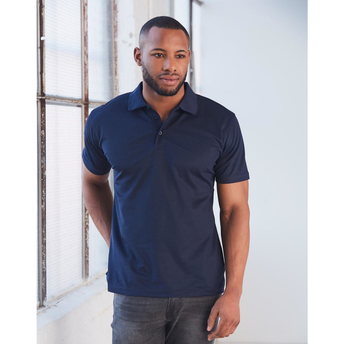A man models a navy blue short-sleeved polo shirt, featuring a collar and a logo on the chest.