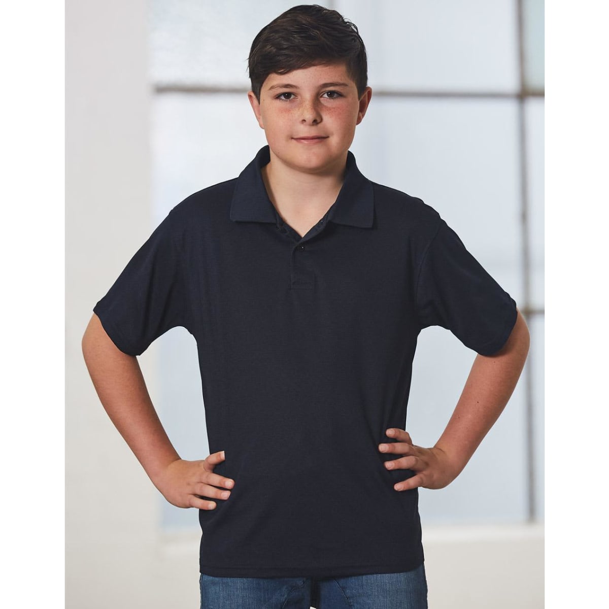 A young boy in a black short-sleeve polo shirt stands confidently with his hands on his hips.