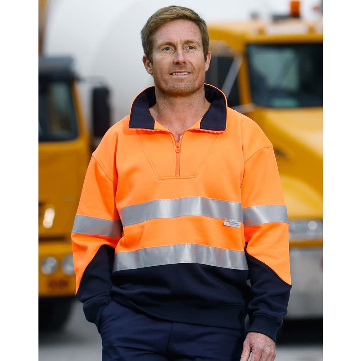 Hi-Vis long-sleeve fleece collar sweater in orange with reflective strips, paired with navy trousers. Features branding.