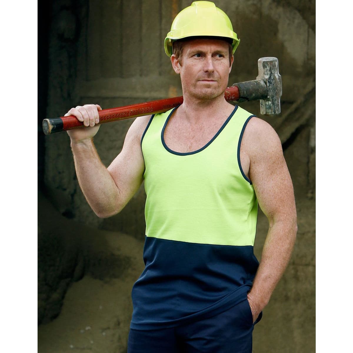 A man wearing a hi-vis yellow and navy safety singlet, holding a hammer over his shoulder, with a hard hat on.