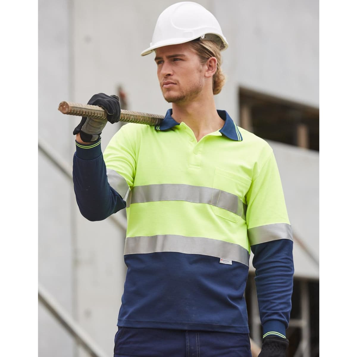 A long-sleeve work polo shirt in high-vis yellow and navy, featuring reflective tape and a pocket. A person wears a hard hat and holds a rod.