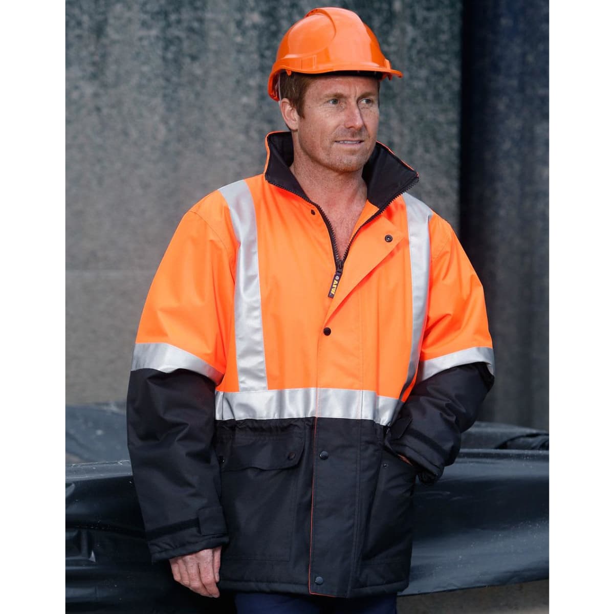 A hi-vis orange and black quilted safety jacket with reflective strips, worn by a person in an orange hard hat.