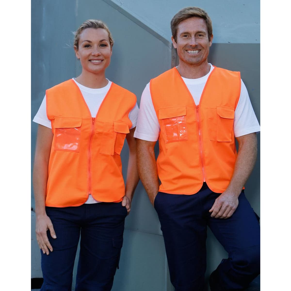 Hi-Vis safety vests in fluorescent orange with ID pockets, worn by two smiling individuals against a grey background.