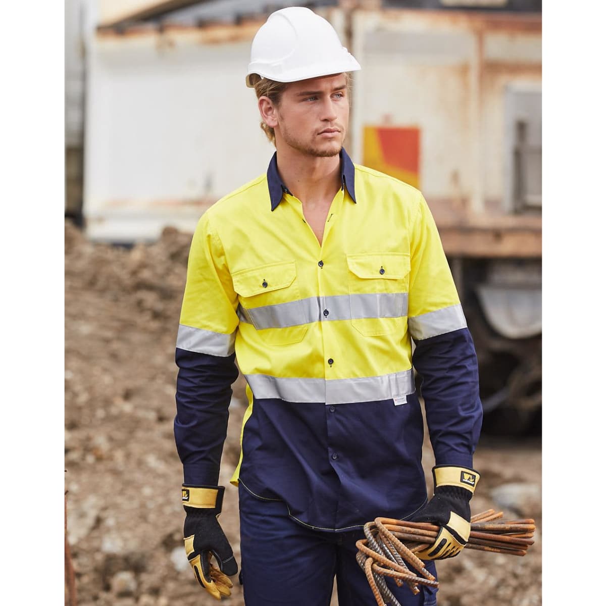 A high-visibility cotton drill shirt in yellow and navy with reflective stripes, worn by a model on a construction site.