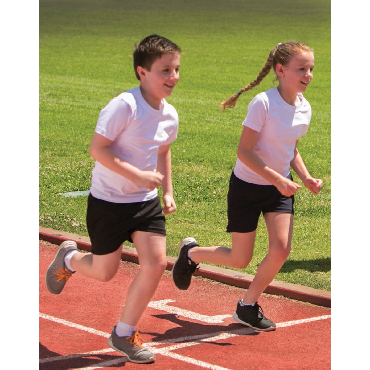 Two children running on a track, wearing white T-shirts and black shorts.