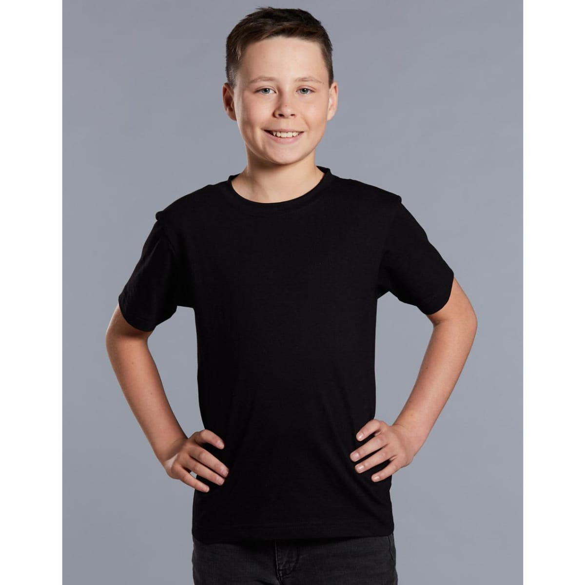 A black semi-fitted cotton t-shirt designed for kids, displayed on a smiling child with hands on hips.