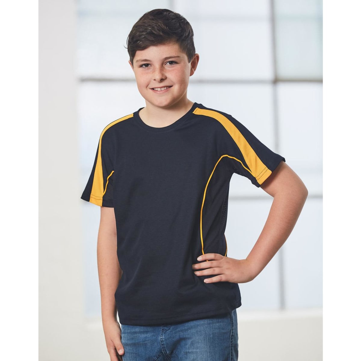 A black and yellow short-sleeved T-shirt featuring a logo, modelled by a smiling boy in front of a bright window.