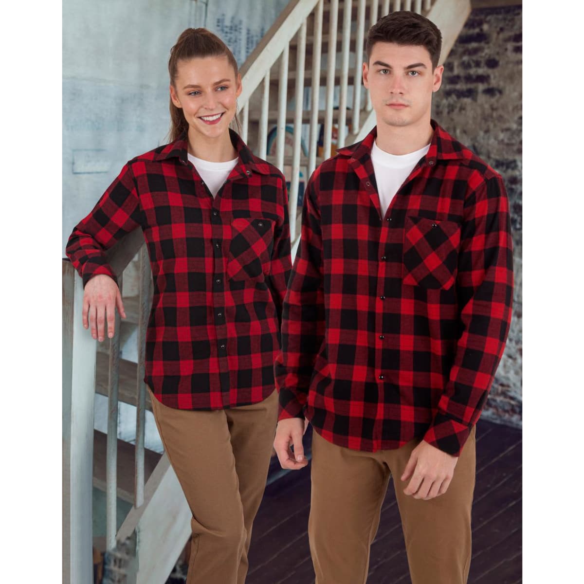 A unisex flannel plaid shirt in red and black, displayed on a male and female model, featuring a logo.